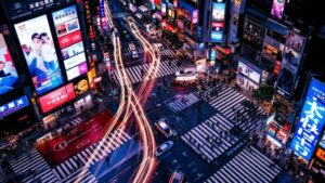 Twilight aerial view of Shibuya Crossing with glowing digital billboards and light trails